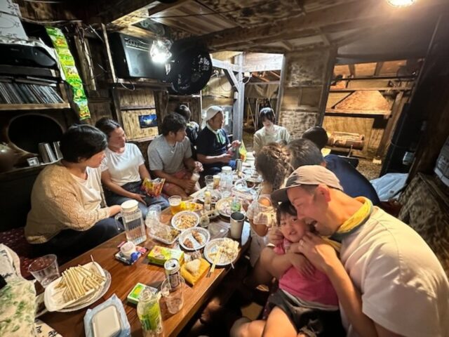 木造の室内で長いテーブルを囲んで食事をするグループ